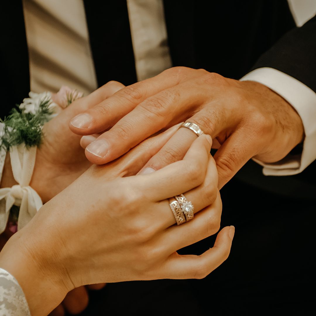 A close up of a bride putting a wedding ring on the groom's hand.